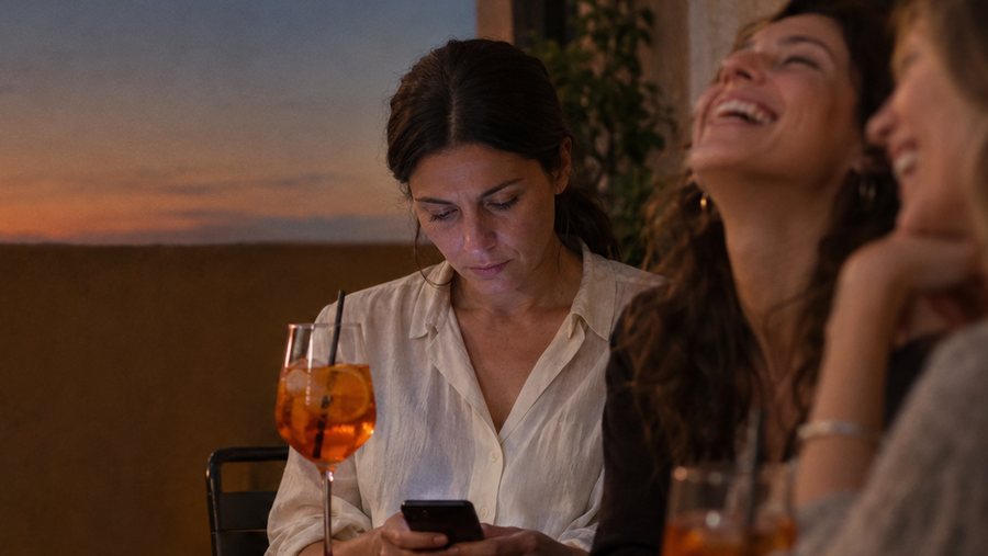 Le amiche ridono, lei guarda il telefono